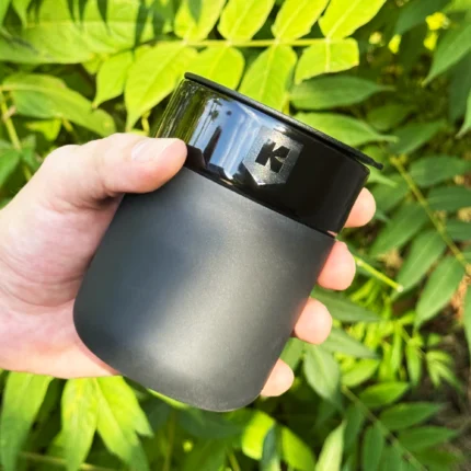 Чорне матове керамічне горнятко Kyiv Digital take-away з лазерним гравіюванням знака в руці на фоні зелені